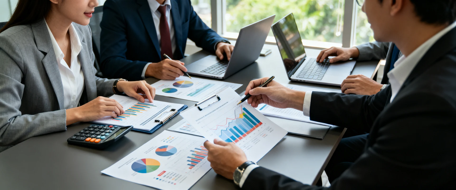 Equipe de negócios diversificada analisando gráficos financeiros e documentos em mesa de conferência com laptop e calculadora, fotografia editorial ultra-realista com luz natural, foco nítido e detalhes precisos em alta resolução.